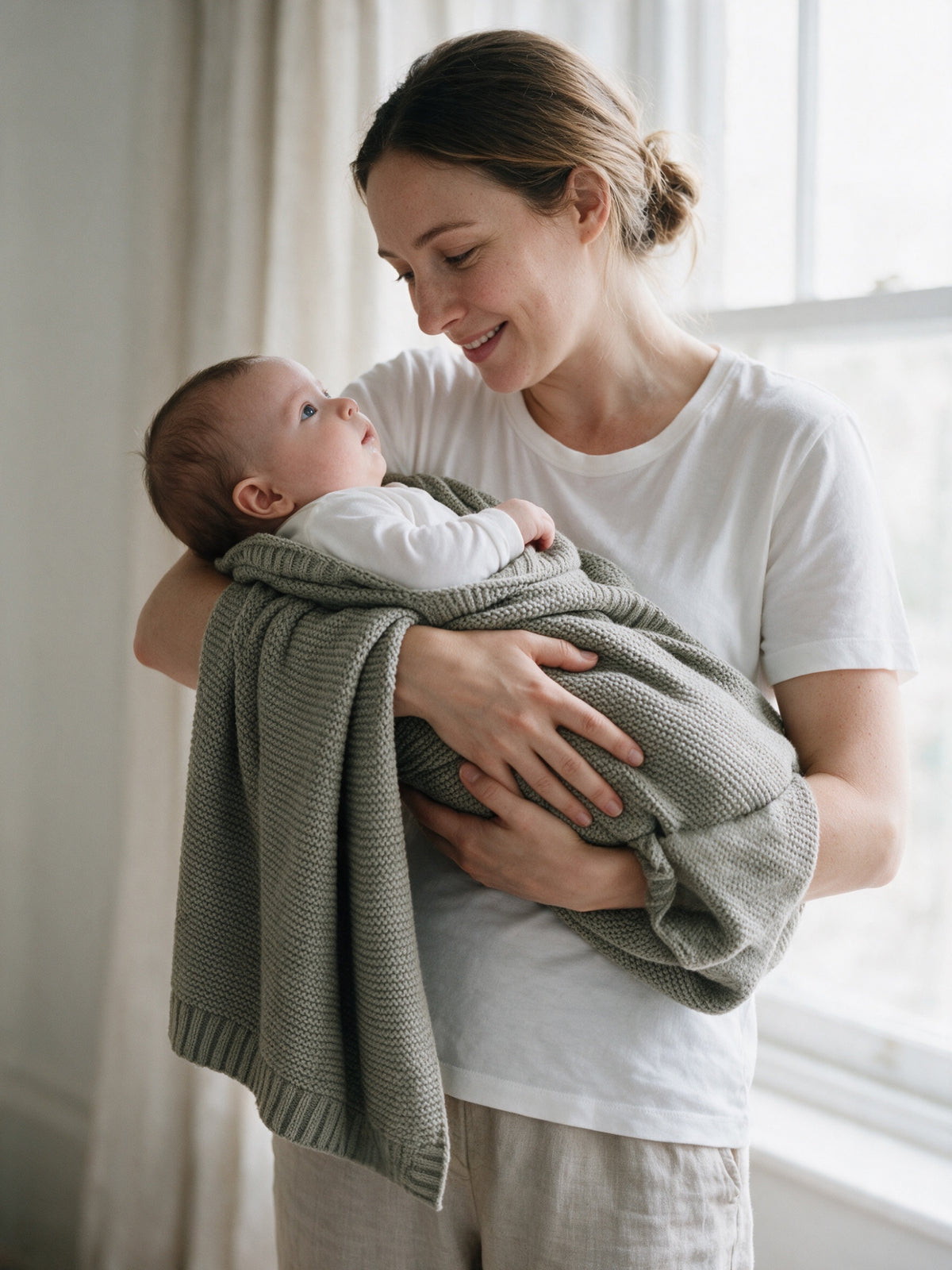 Mother holding her baby wrapped in a Sage knitted blanket